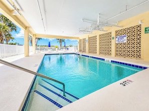 An indoor swimming pool with a 3ft depth marker, a lifeguard duty sign, and a view of palm trees outside.