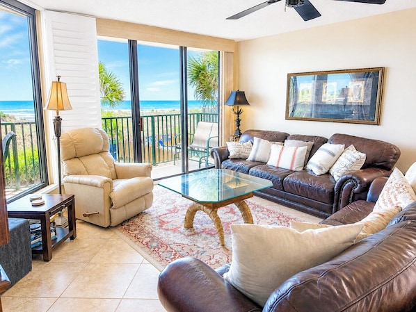 A living room with a glass coffee table, leather sofas, and a view of the beach.