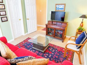 A living room with a red sofa, a glass coffee table, a wooden cabinet with a television on top, and a patterned rug.