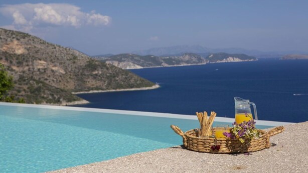 A wicker basket with snacks and a drink on a terrace overlooking a clear blue sea and a mountainous landscape. - Villa Fyki (Lefkada)