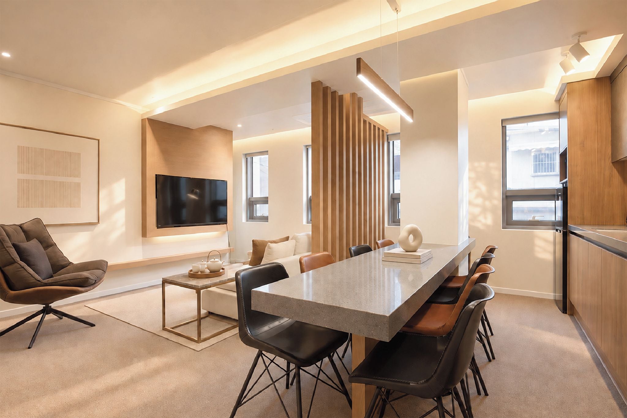 A modern living room with a flat-screen TV, a sofa, a coffee table, and a dining area with a long table and chairs.