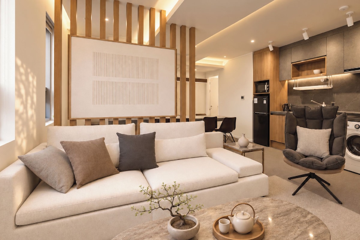 A modern living room with a sofa, a coffee table with a plant, and a kitchen area with appliances.