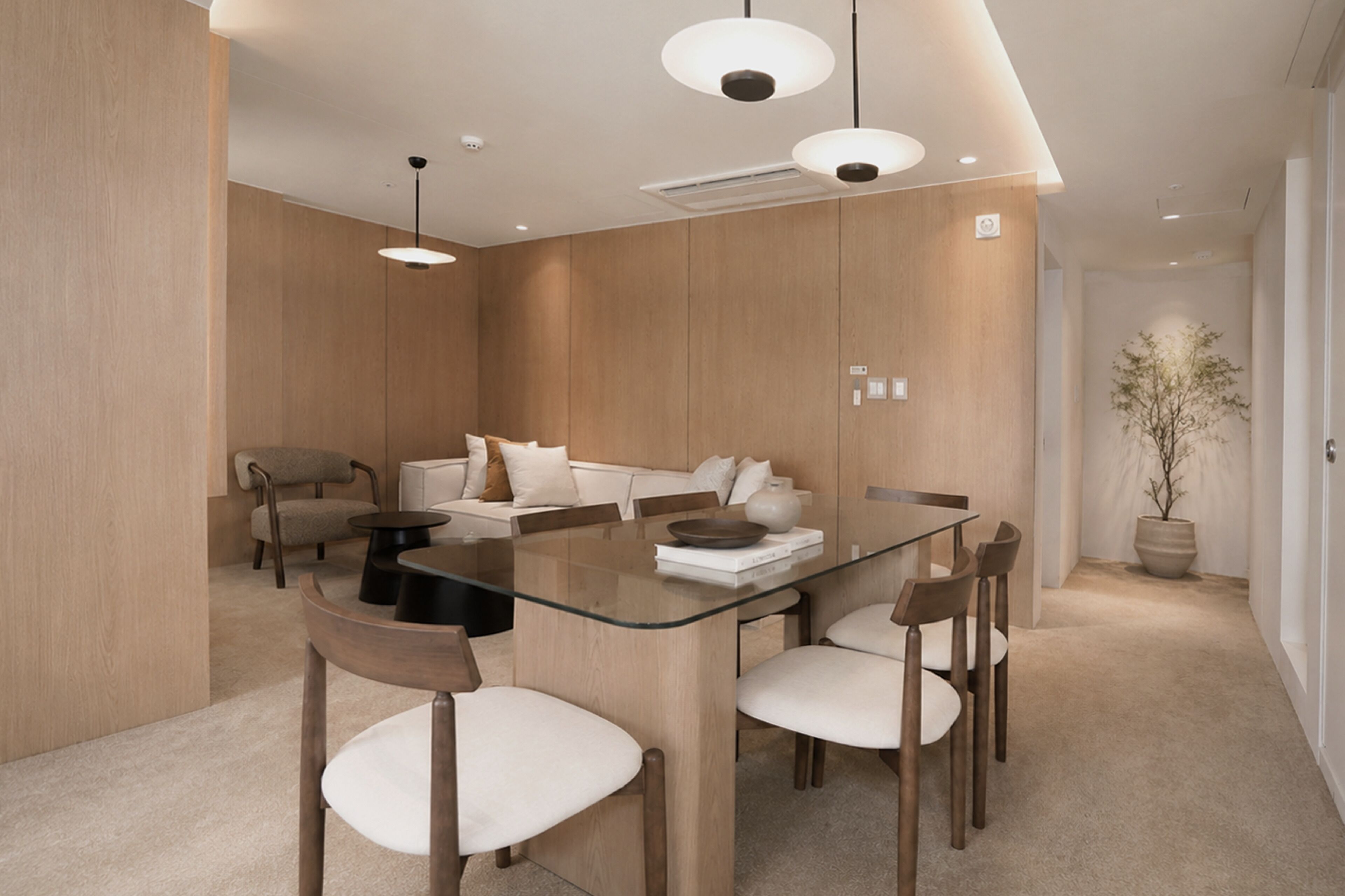 A modern dining area with a glass table, wooden chairs, a sofa, and pendant lighting.