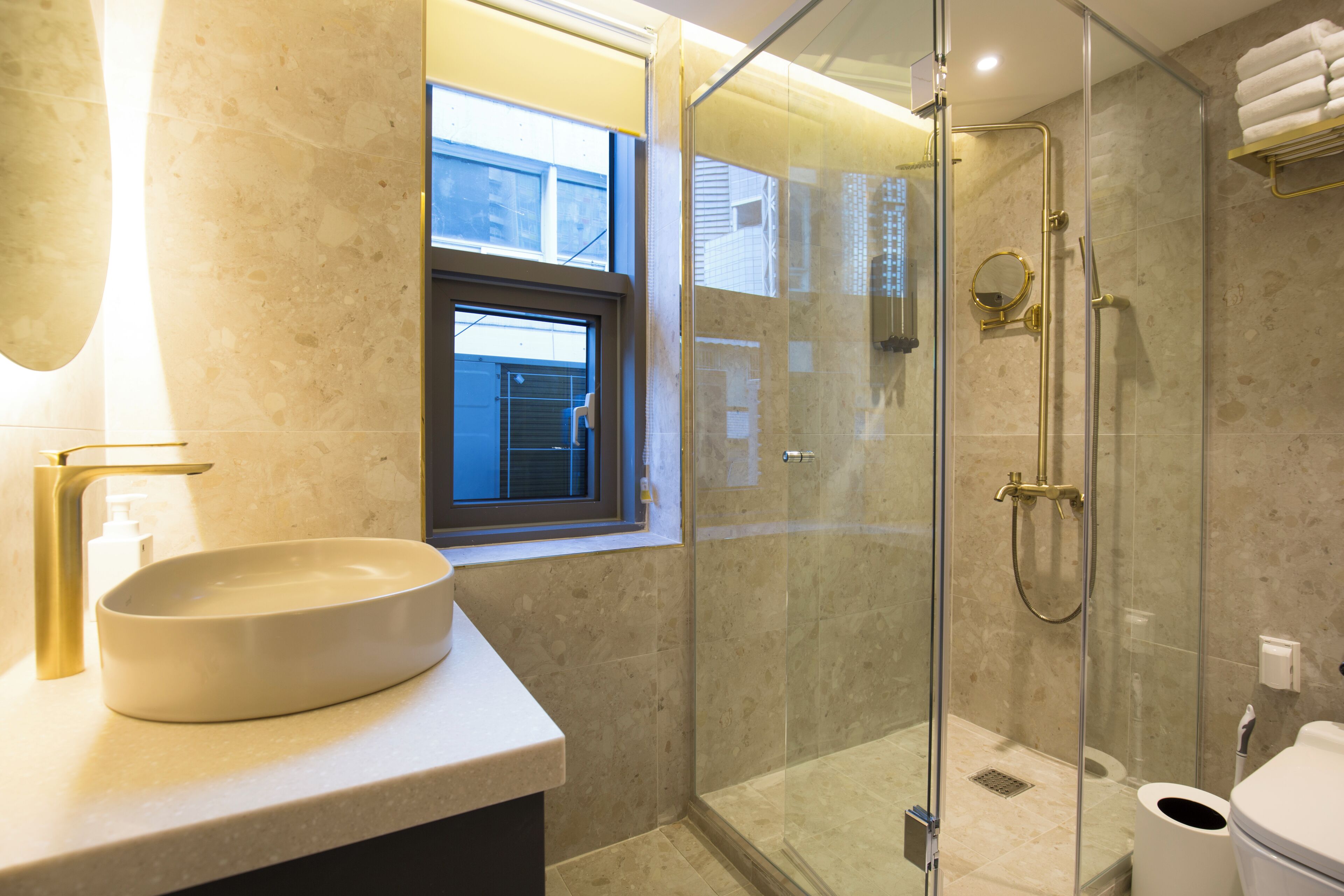 Un baño moderno con un lavamanos ovalado grande, una ducha con cerramiento de vidrio y una ventana que proporciona luz natural.
