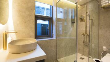 Un baño moderno con un lavamanos ovalado grande, una ducha con cerramiento de vidrio y una ventana que proporciona luz natural.