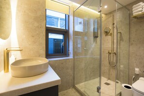 Un baño moderno con un lavamanos ovalado grande, una ducha con cerramiento de vidrio y una ventana que proporciona luz natural.