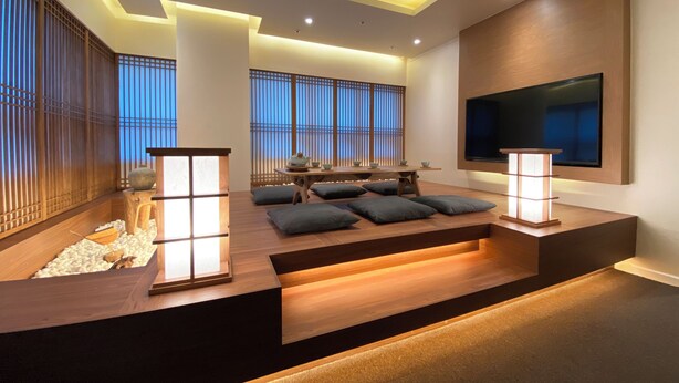 Una sala moderna con piso de madera, un televisor de pantalla plana en la pared, una mesa de centro de madera y una zona de estar con cojines.