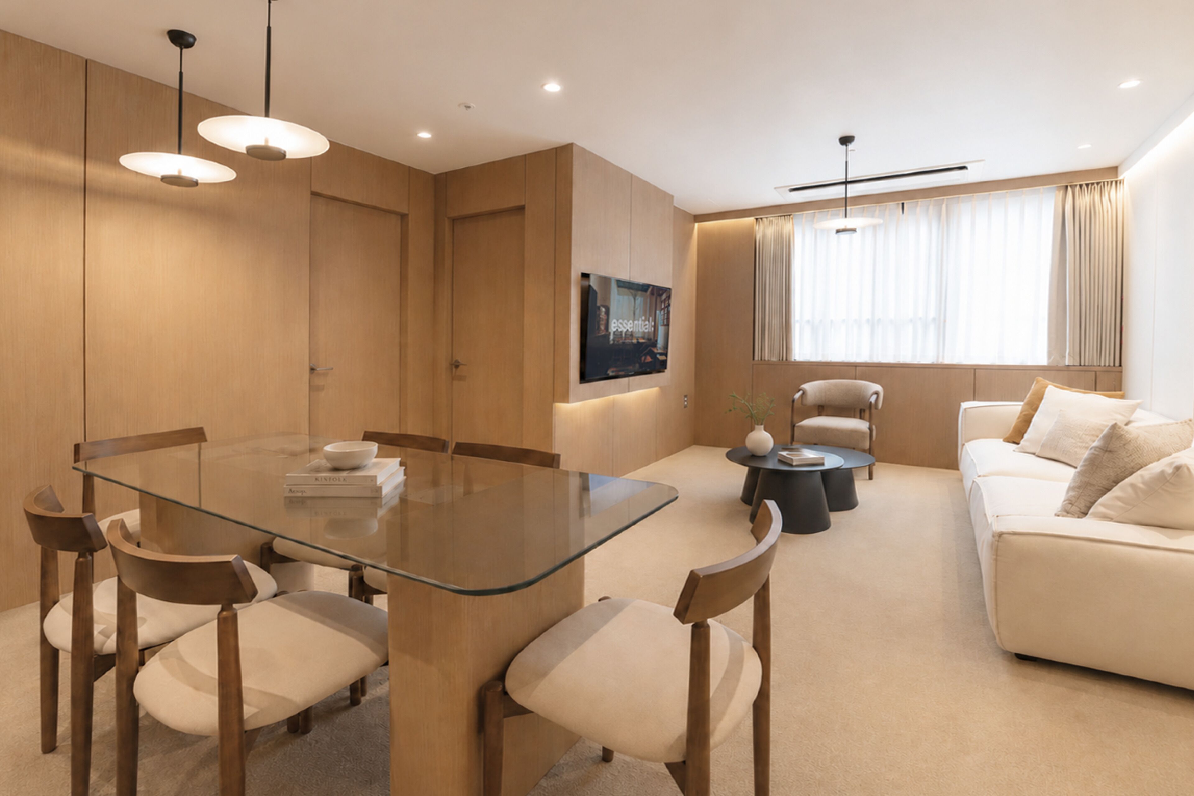 A modern living room with a glass dining table, wooden chairs, a sofa, and a TV mounted on the wall.