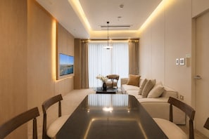 A modern hotel room with a large dining table, a sofa, a TV mounted on the wall, and a large window with curtains. - UH Suite The Jongno (Seoul)