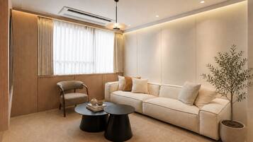 A modern living room with a sofa, two side tables, a chair, a potted plant, and a window with curtains.