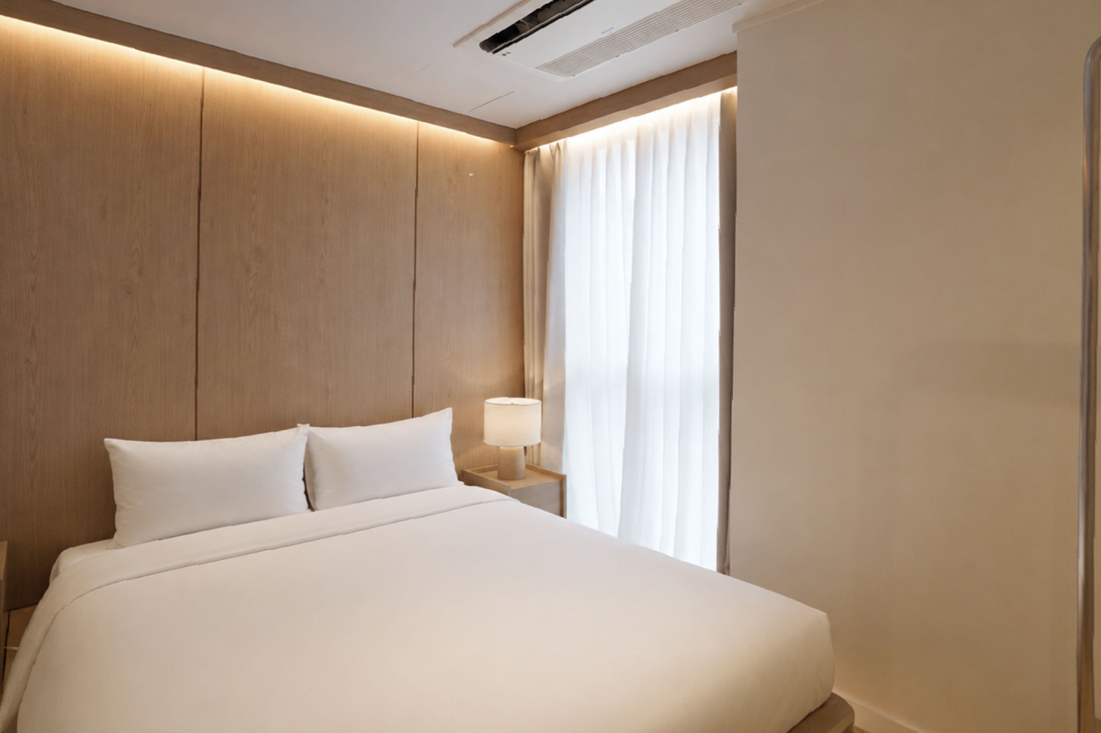 Ein Hotelzimmer mit einem großen Bett, einem Nachttisch mit Lampe und einem Fenster mit Vorhängen.