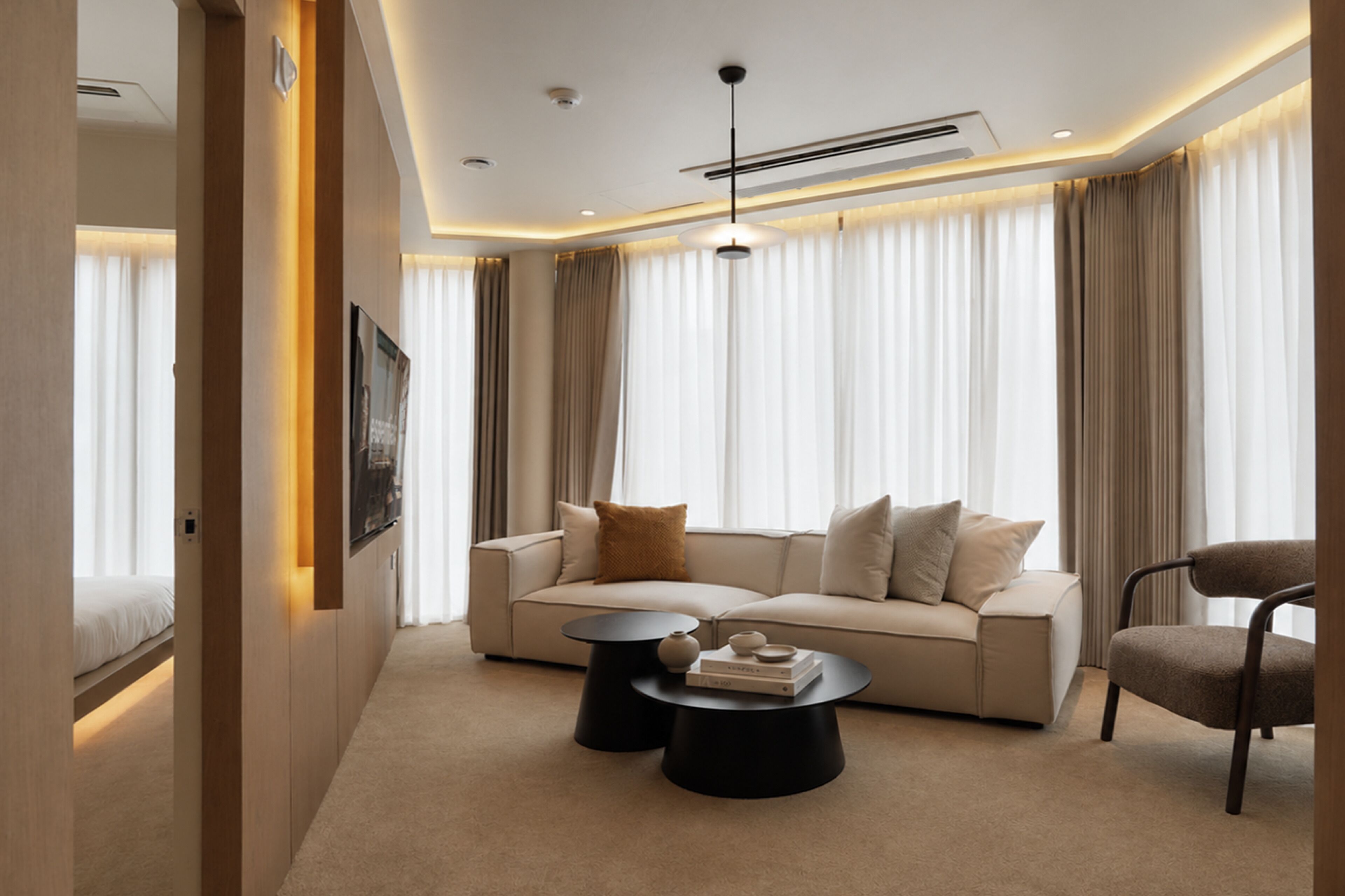 A modern living room with a sofa, two black coffee tables, a single chair, and a ceiling-mounted light fixture.