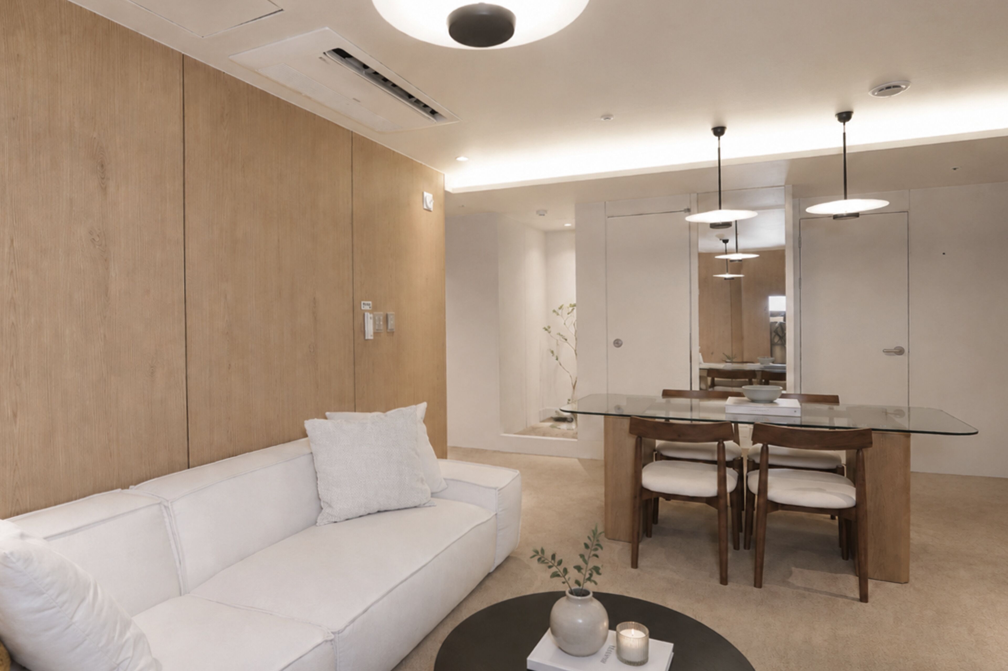 A modern living room with a white sofa, a glass dining table with chairs, and a coffee table with a vase and candle.