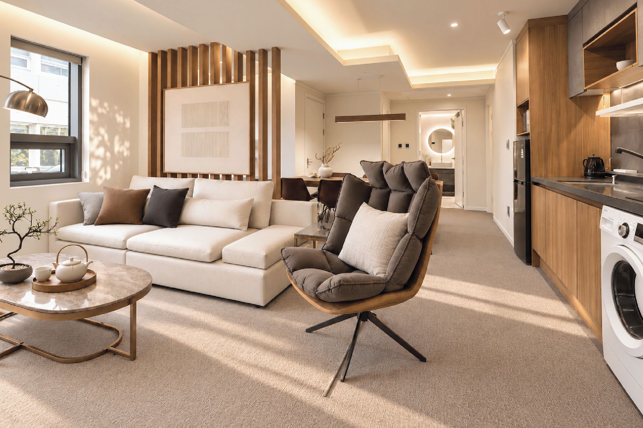 A modern living room with a sofa, armchair, and coffee table. There is a kitchen area with a washing machine and cabinets.