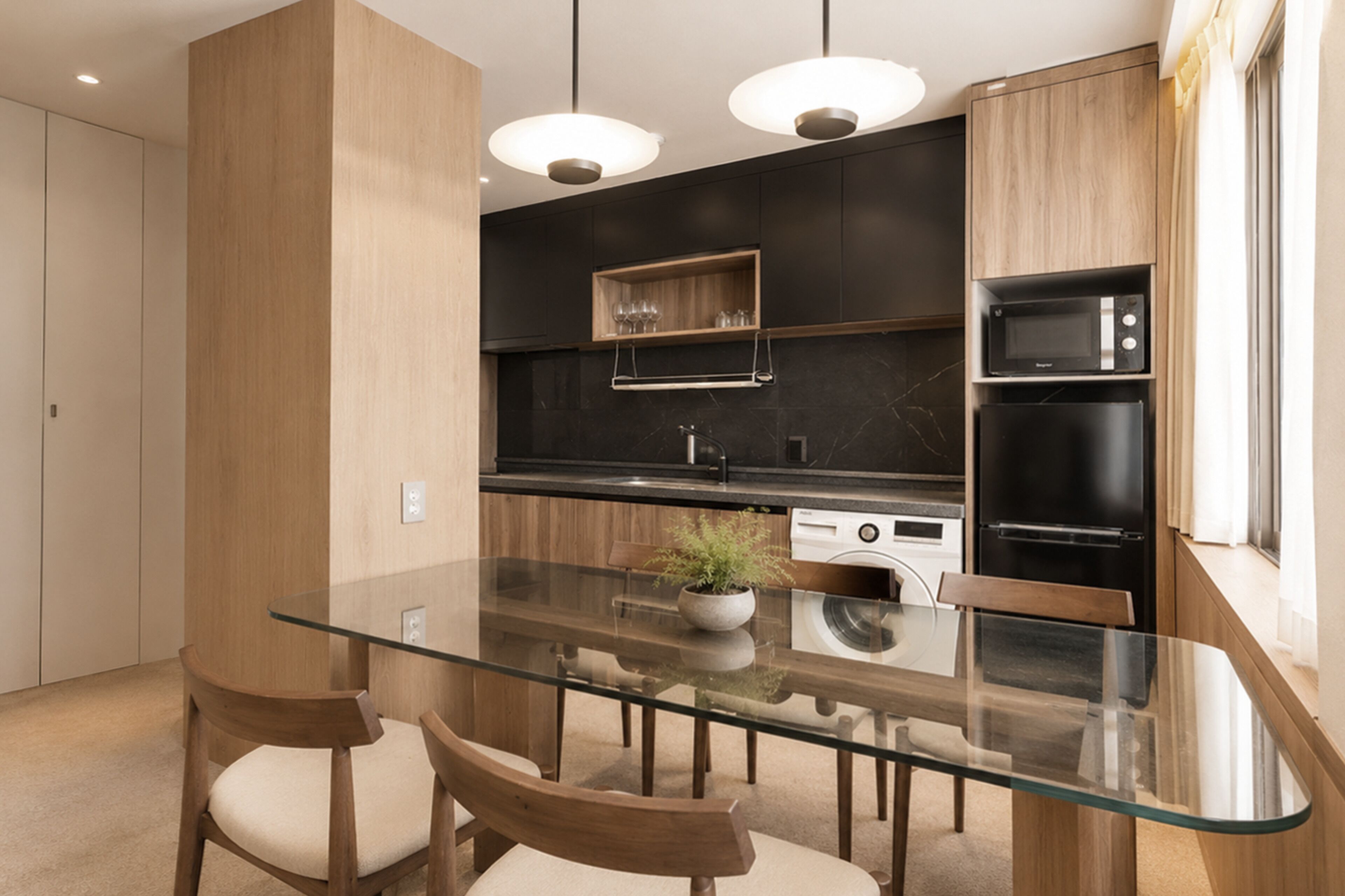A modern kitchen with a glass dining table, wooden chairs, a built-in oven, and a microwave.
