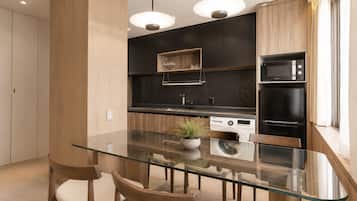 A modern kitchen with a glass dining table, wooden chairs, a built-in oven, and a microwave.