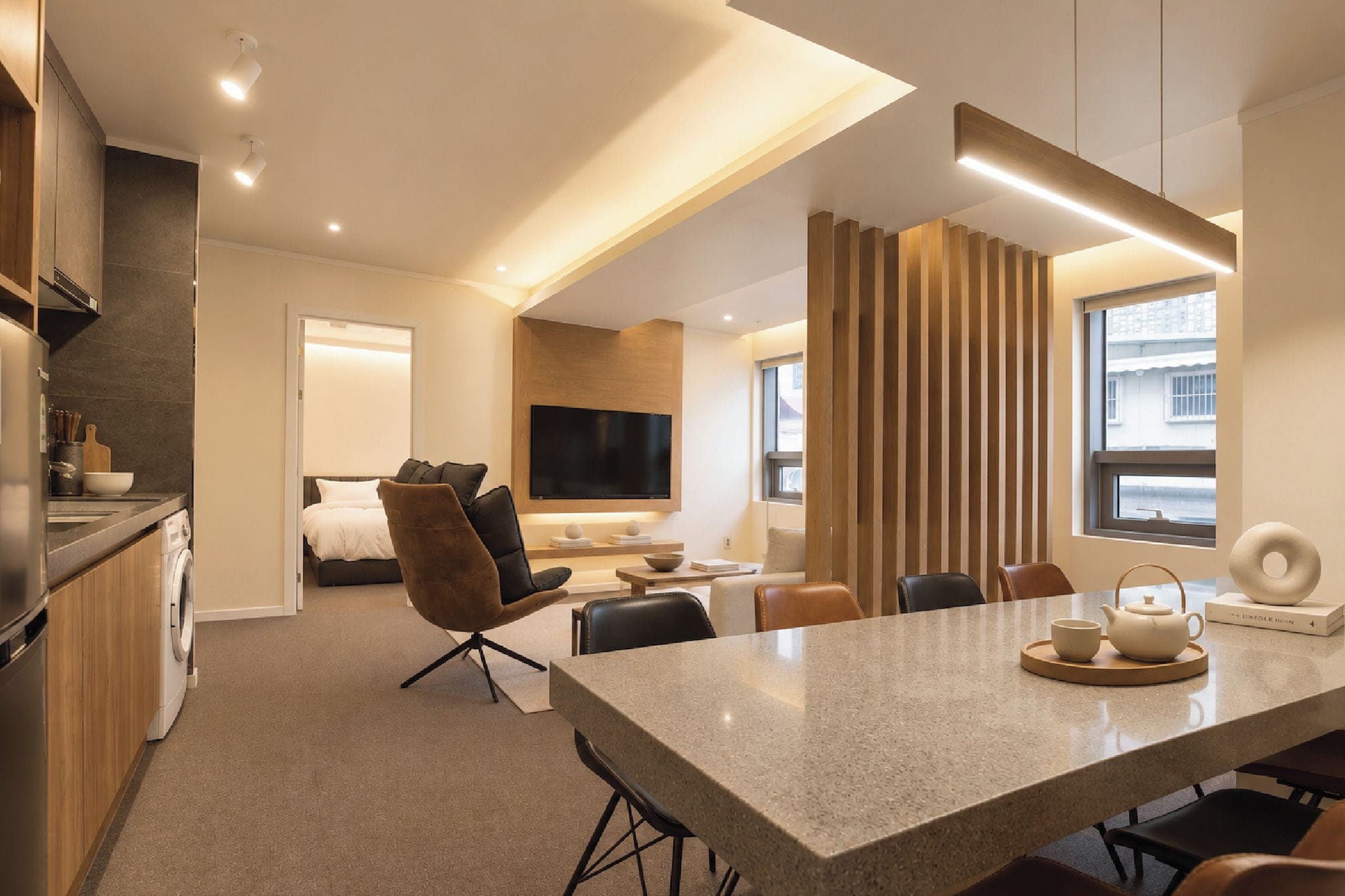 A modern hotel room with a kitchen, dining area, and a separate bedroom.