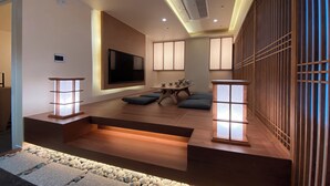 Una sala de estar moderna con una televisión de pantalla plana montada en la pared, una mesa de centro de madera y un área de descanso con cojines.