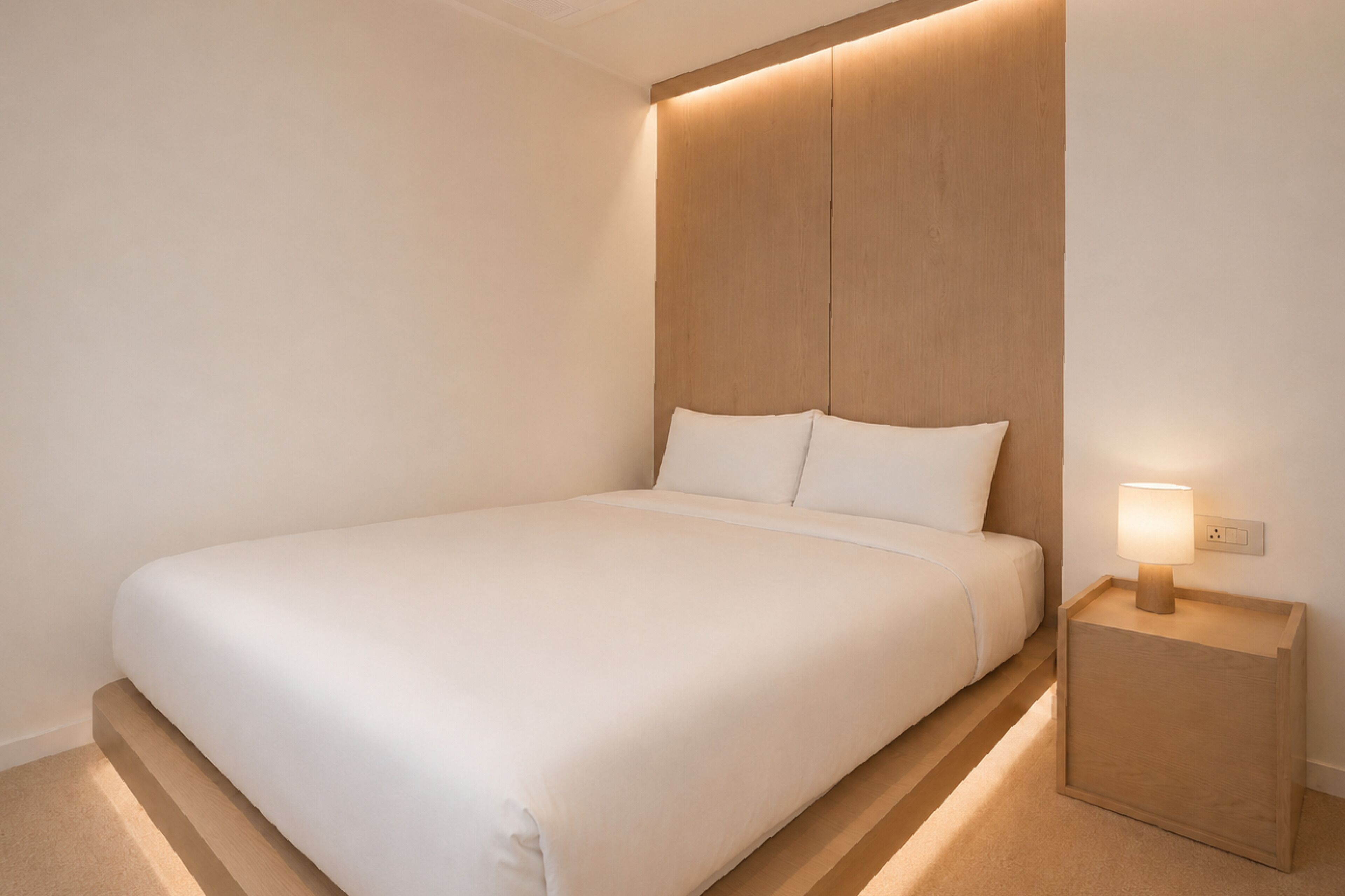 Un lit bien fait, avec une tête de lit en bois, une table de chevet avec une lampe et une prise électrique au mur.