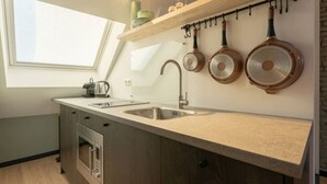 Moderni keittiö, jossa on kattovalokuvio, ruostumattomasta teräksestä valmistetut kodinkoneet ja seinälle ripustettavat keittoastiat.