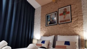 Hotellihuone, jossa on sänky, kattotuuletin, tiiliseinä ja kaksi kehystettyä kuvaa.