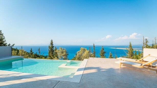 Zona de piscina con vista al mar, sillones de madera y cielo despejado.