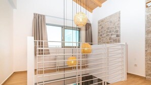 Una habitación con un separador metálico blanco, una ventana con cortinas, un muro de piedra y una lámpara colgante de tejido.