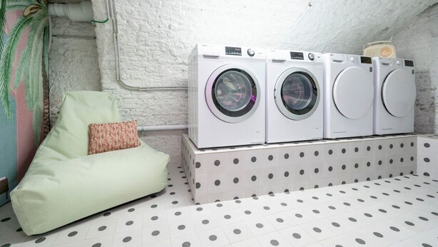 Une buanderie avec trois machines à laver superposées, un sol à motifs à pois et un canapé vert agrémenté d’un coussin à motifs.