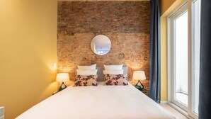 A hotel room with a brick wall, a large bed with white bedding, two bedside lamps, and a window with curtains. - The Red Monkey by SHWAY (Antwerpen)