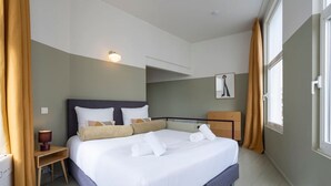 Et hotelværelse med en stor seng, et natbord med lampe, et skab, og et vindue med gardiner.