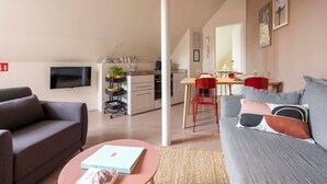 A modern living room with a grey sofa, a red chair, and a flat-screen TV mounted on the wall. - The Suit by SHWAY Antwerp (Antwerpen)