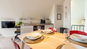 A modern kitchen with a dining area, including a wooden table set with plates, glasses, and a TV mounted on the wall. - The Suit by SHWAY Antwerp (Antwerpen)