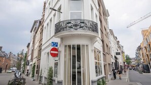 A corner building with a white facade, multiple windows, and a balcony with intricate metalwork. - The Suit by SHWAY Antwerp (Antwerpen)