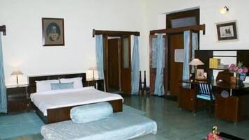 Quarto de hotel com uma cama grande, uma mesa, uma cadeira e uma pequena mesa com abajur.