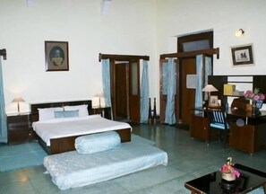 Una habitación de hotel con una cama grande, un escritorio, una silla y una mesita con una lámpara.