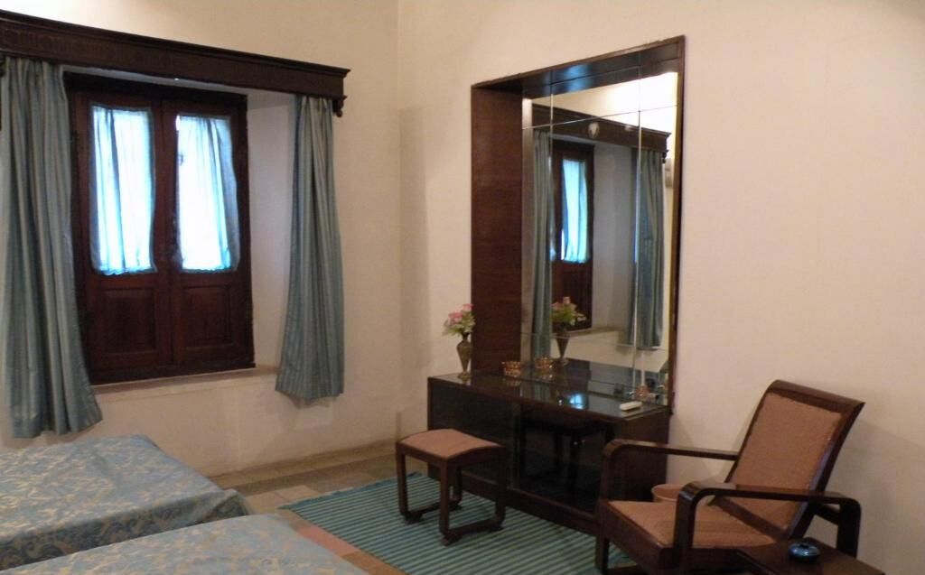 Habitación de hotel con dos camas individuales, una mesita con una silla, un espejo y una ventana con cortinas.