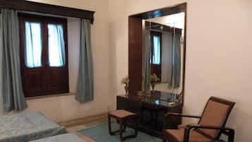 Habitación de hotel con dos camas individuales, una mesita con una silla, un espejo y una ventana con cortinas.