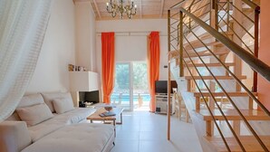 A modern living room with a sofa, a coffee table, and a TV. There is a staircase with wooden railings leading to an upper level. - Villa Niriides (Lefkada)