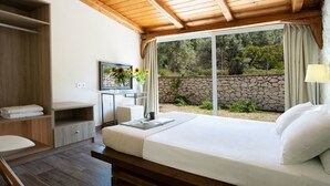 A bedroom with a large bed, a desk, a chair, and a window with a view of greenery. - Villa Niriides (Lefkada)