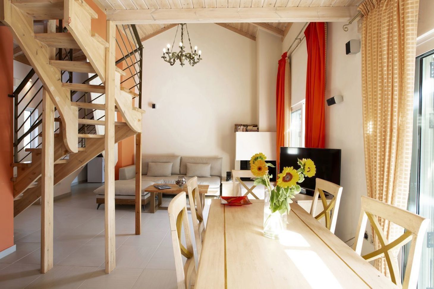 Un vaste espace de vie comprenant un escalier en bois, une table à manger avec des chaises, un canapé, un téléviseur et un lustre.