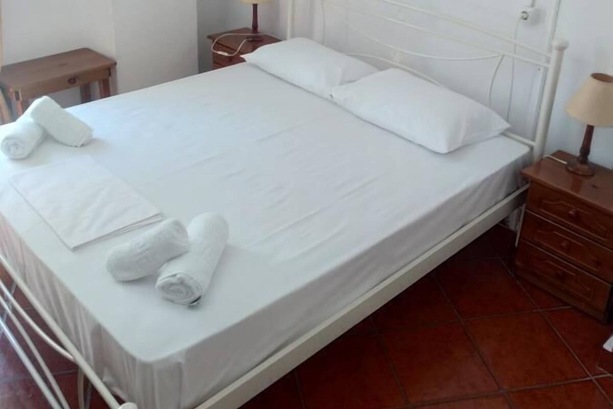 A neatly made bed with white linens and towels, a bedside table with a lamp, and a wall-mounted air conditioning unit.