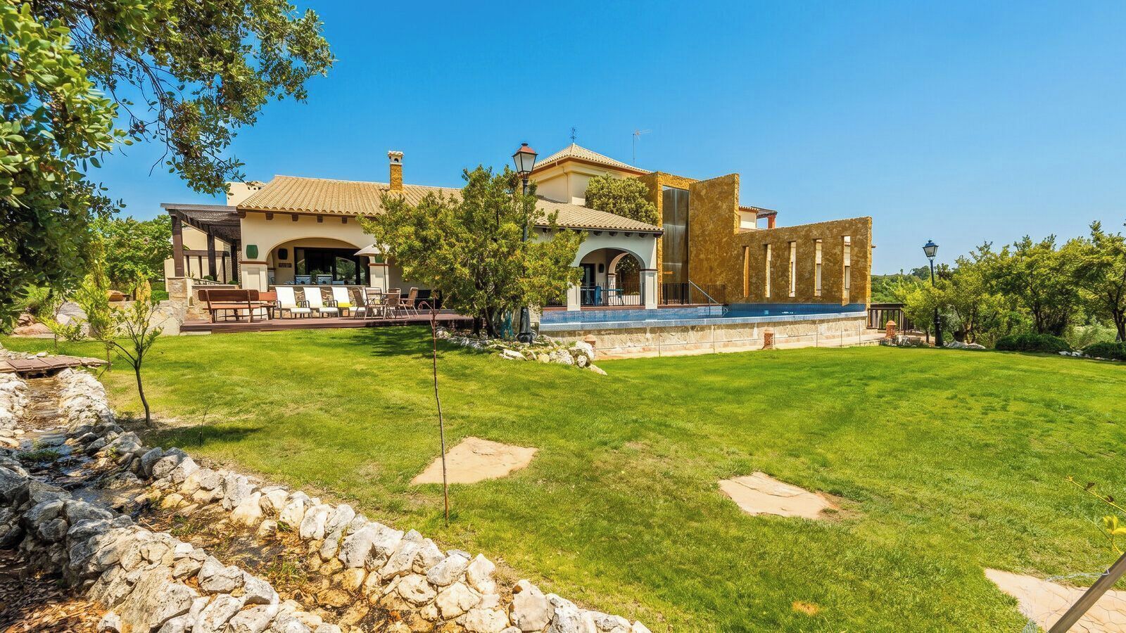 Une grande maison dotée d’un patio, d’un mur en pierre et d’une pelouse bien entretenue.