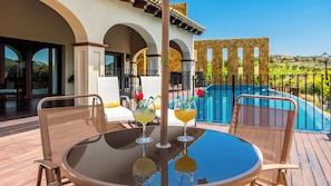 A poolside area with a table, chairs, and two cocktails.