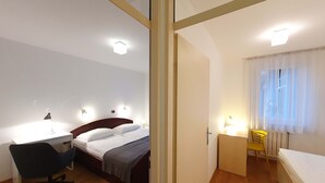 Et hotelværelse med seng, natbord, lampe, stol og et lille skrivebord med tilhørende stol.