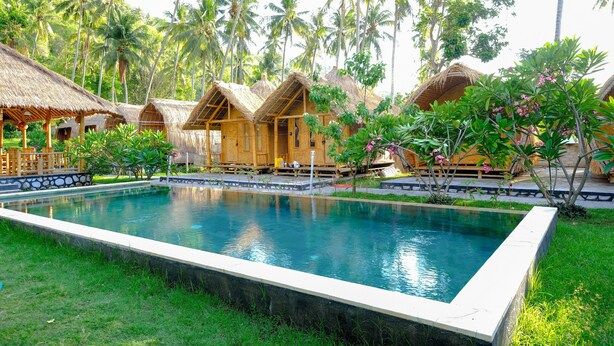 A pool surrounded by thatched-roof huts, palm trees, and lush greenery. - OYO 2039 Cici's Bungalow (Senggigi)
