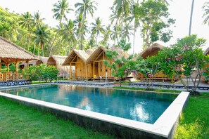 A pool surrounded by thatched-roof huts, palm trees, and lush greenery. - OYO 2039 Cici's Bungalow (Senggigi)