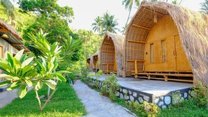 A row of thatched-roof cottages with a stone pathway leading to them, surrounded by lush greenery. - OYO 2039 Cici's Bungalow (Senggigi)