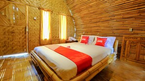 A room with a bamboo-themed interior, including a bed with red and white bedding, a wooden headboard, and a woven wall design. - OYO 2039 Cici's Bungalow (Senggigi)