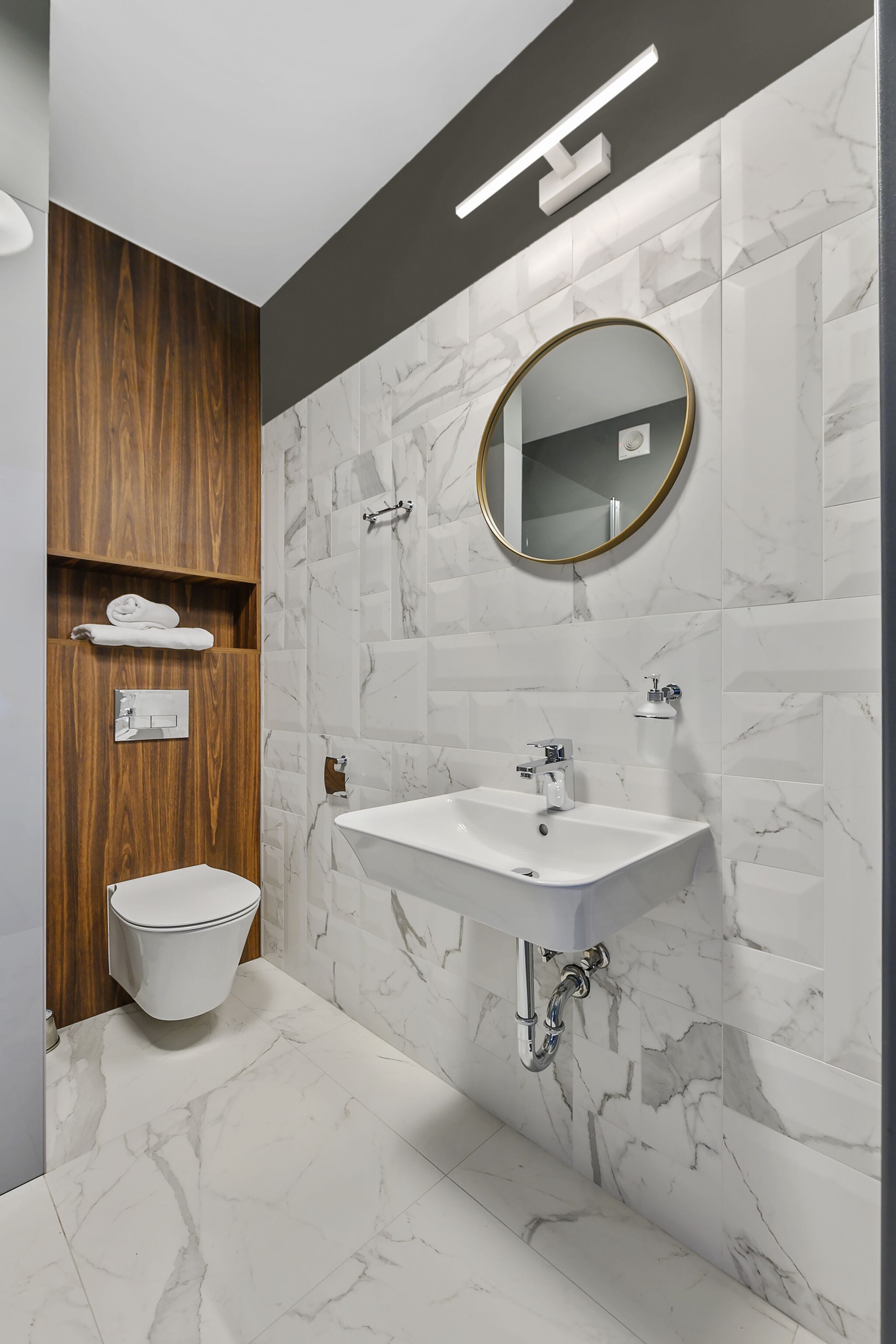 Un baño moderno con lavamanos blanco, estanterías de madera, un inodoro y paredes con diseño de mármol.