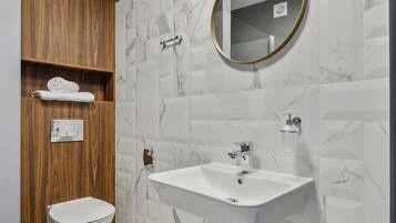 Un baño moderno con lavamanos blanco, estanterías de madera, un inodoro y paredes con diseño de mármol.